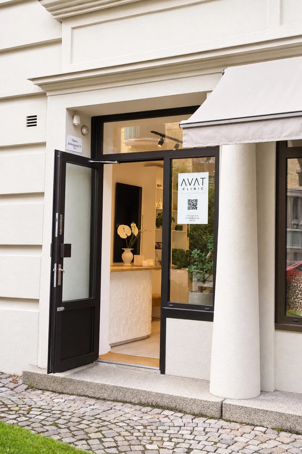 Öppen ytterdörr till Avat Clinic på Arkivgatan 5, med kullersten utanför