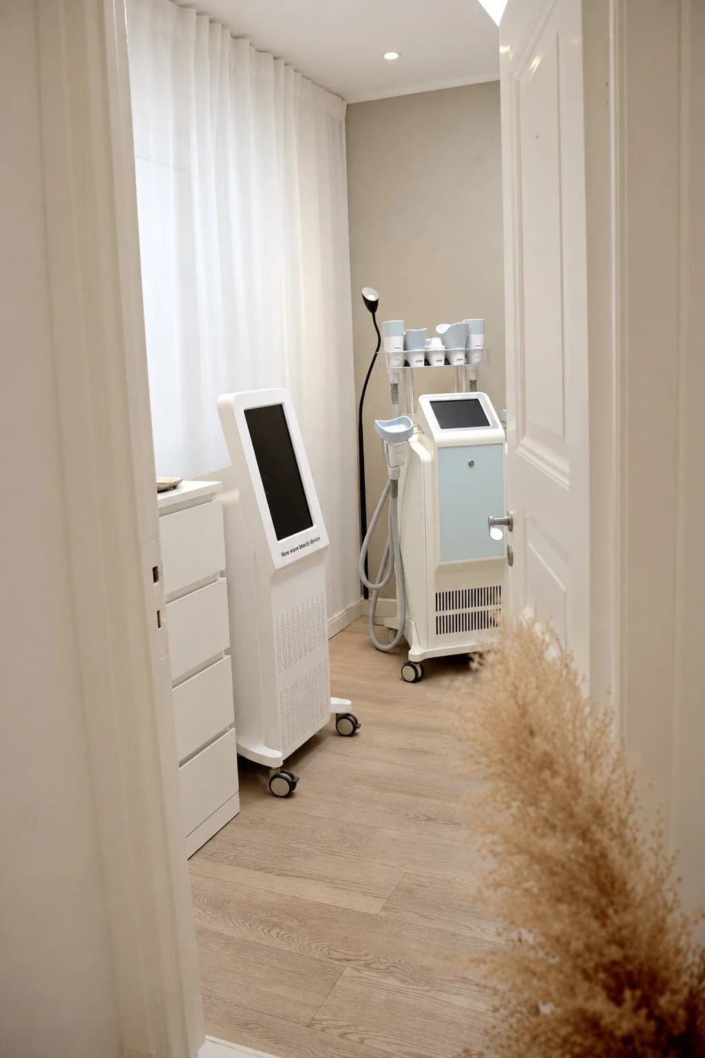 Behandlingsrum hos Avat Clinic med behandlingsapparat på hjul och pampasgräs i hörnet